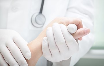 Ein Arzt hält mit bekleideten Händen die Hand eines Patienten. Seine Hände sind bekleidet mit weißen Einmalhandschuhen