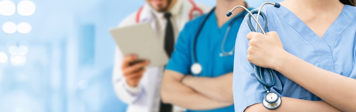 im Hintergrund ein unscharfer Flur, dann ein Arzt in weißem Kittel, ein Mediziner in blauem Dress, eine Ärztin in hellblauem Dress